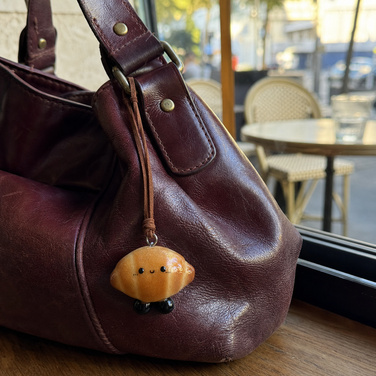 Croissant Buddy Charm, a handmade real bread bag charm by Doubie Dough, clipped onto a natural leather bag