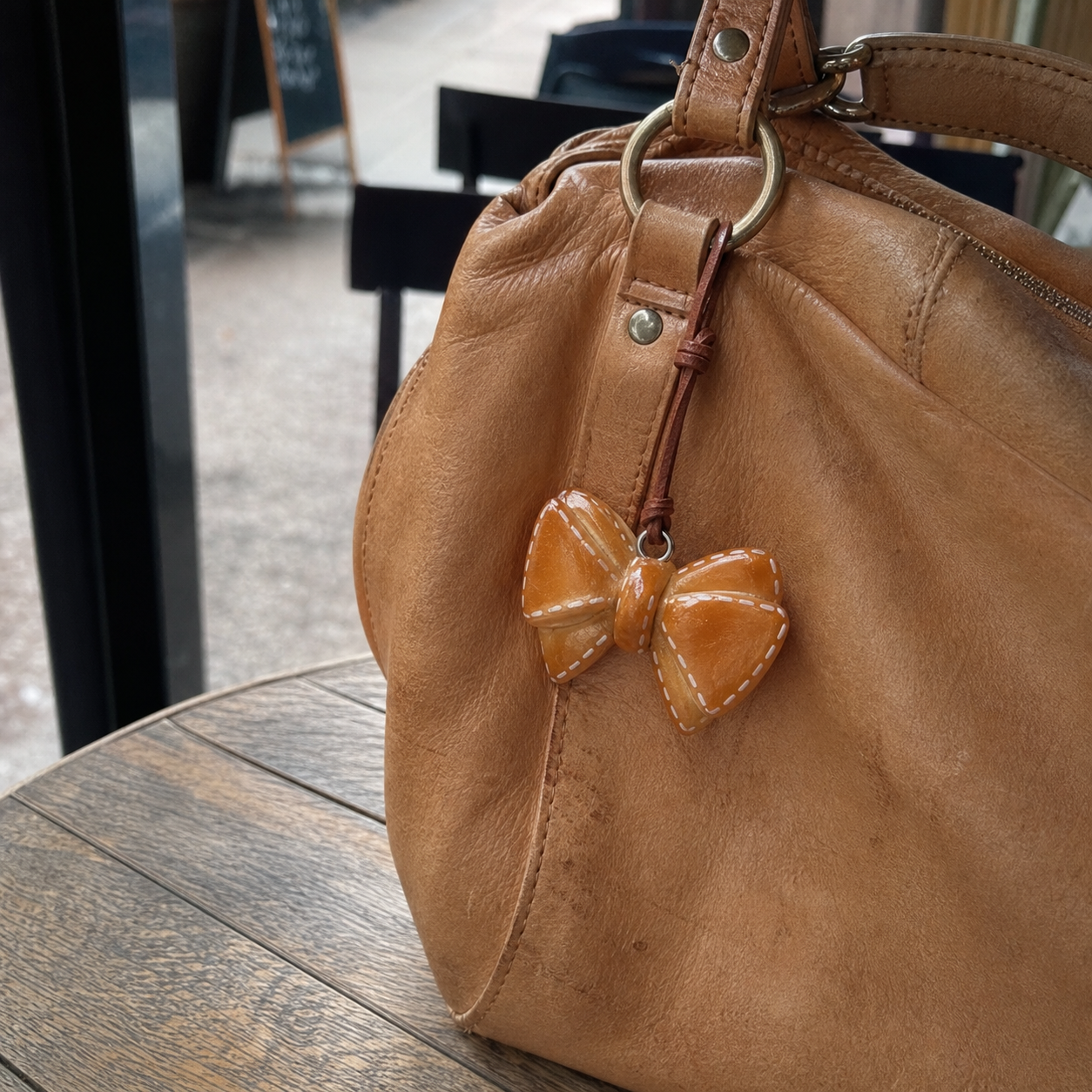 Golden bow bread bag charm displayed on a natural leather handbag