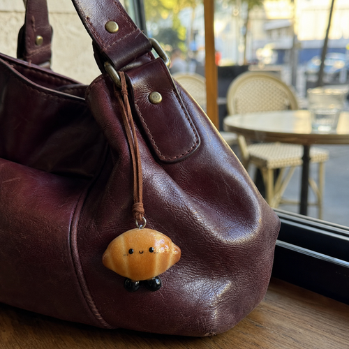 Croissant Buddy handmade real bread charm hanging from a natural leather handbag