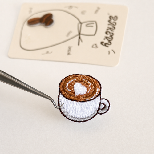 Embroidered coffee cup sticker patch held with tweezers