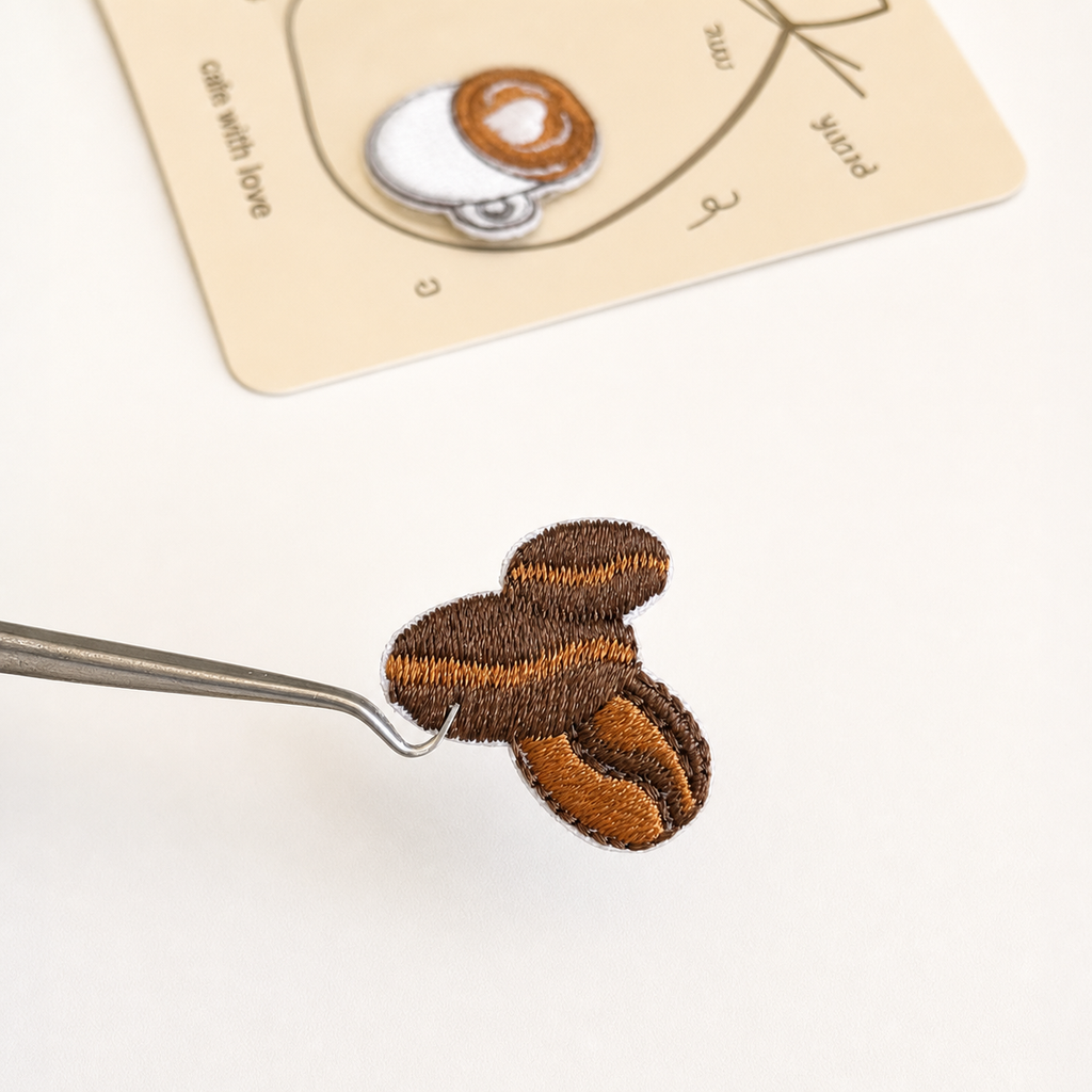 Coffee bean embroidered sticker patch held with tweezers