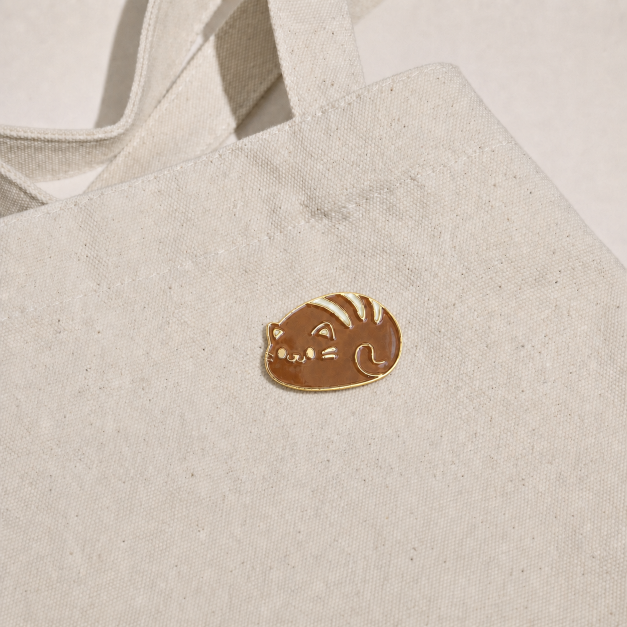 Cat Bread Pin displayed on a natural canvas tote bag